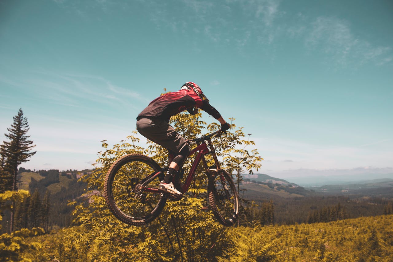 Mountain biker flying through the air against a picturesque backdrop of lush greenery and blue skies.