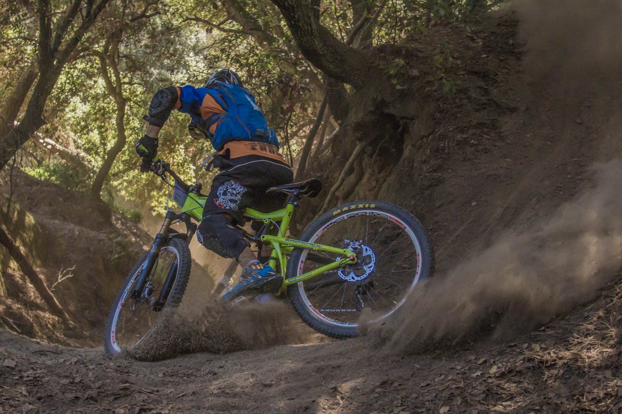 Mountain biker navigates a challenging off-road trail, kicking up dust in a forest setting.